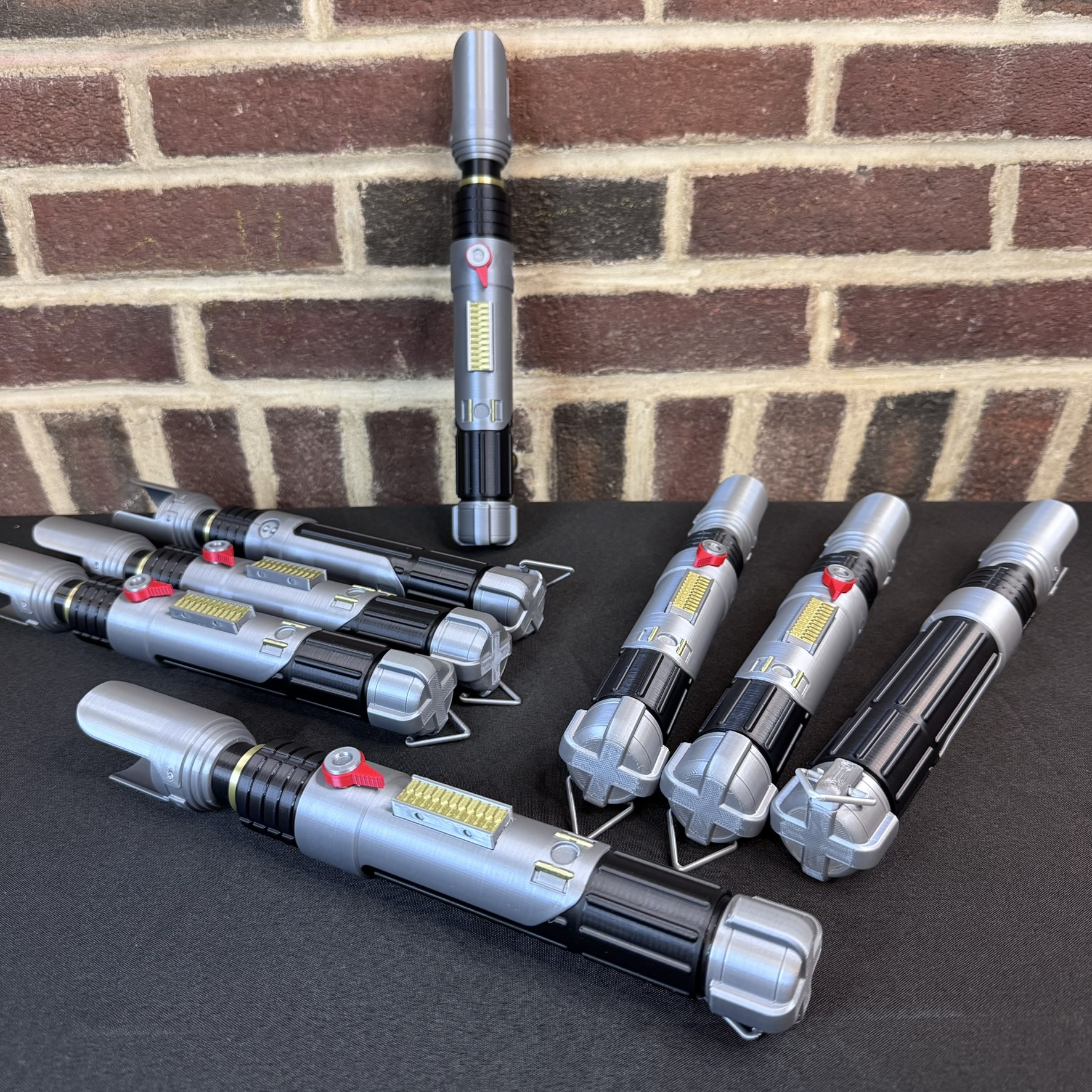 Group of Sabine Wren lightsaber replica hilts displayed on a table with silver, black, and red detailing.