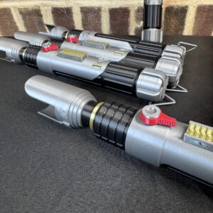 Group of Sabine Wren lightsaber replica hilts displayed on a table with silver, black, and red detailing.
