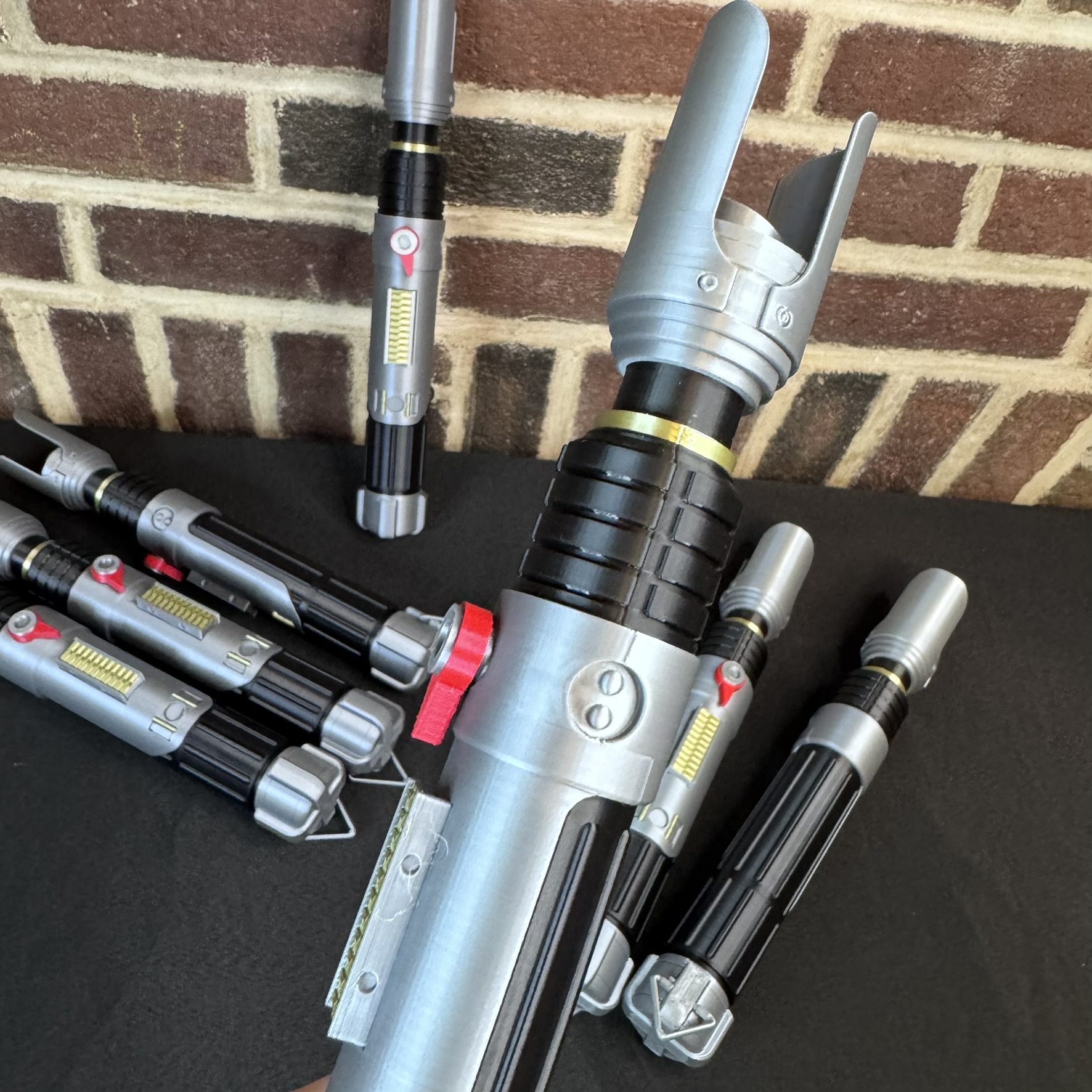 Sabine Wren–inspired lightsaber hilts arranged on a black tabletop showing detailed red, gold, and silver accents.