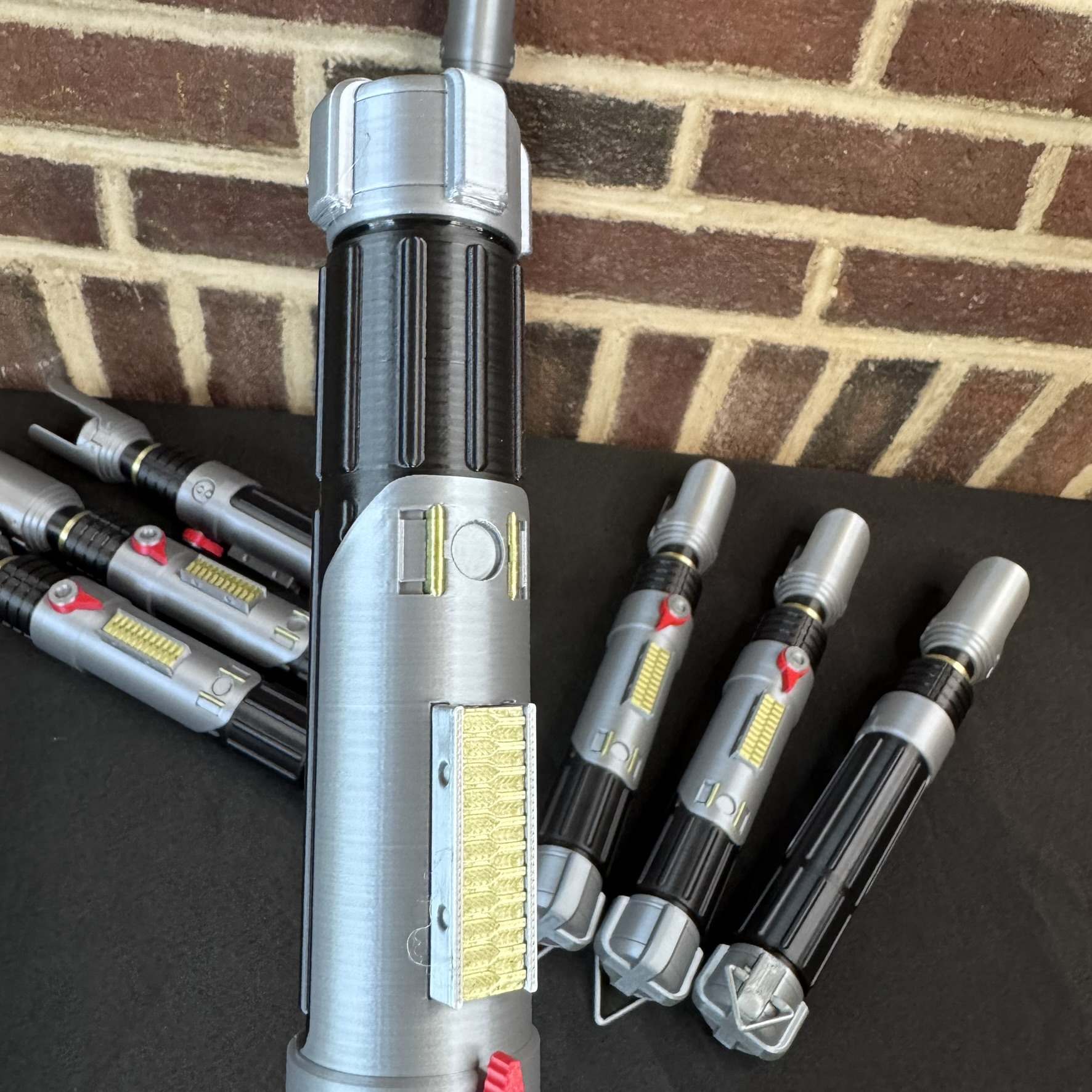Sabine Wren–inspired lightsaber hilts arranged on a black tabletop showing detailed red, gold, and silver accents.